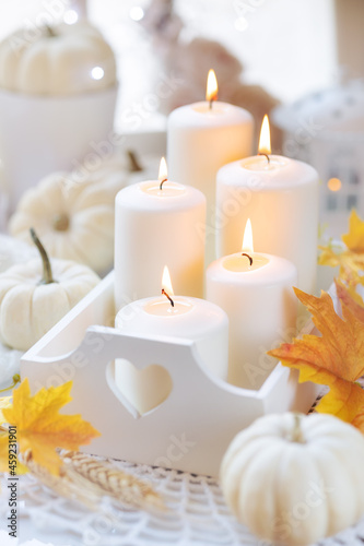 Hello Autumn or Happy Thanksgiving concept with a beautiful cozy composition of burning candles and decorative white pumpkins and autumnal leaves. Shallow depth of field