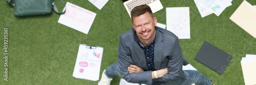 Fotografija Young successful businessman confidently looks up on green lawn lie business cha