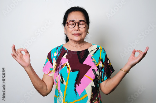 Elderly Asian woman doing meditation pose gesture with eye closed isolated on white background photo