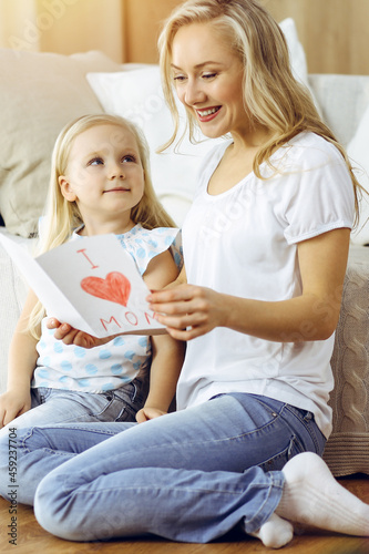 Happy mother day in sunny flat. Child daughter congratulates mom and gives her postcard with heart drawing. Family concept