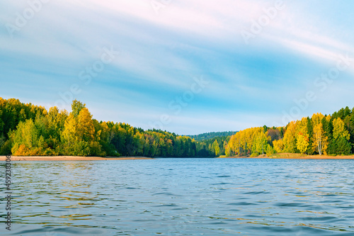 Panoramic view of the bright colorful trees along the bank of the Kama River Russia Perm Krai. Autumn colored trees and blue sky  reflected in the calm and shiny water.