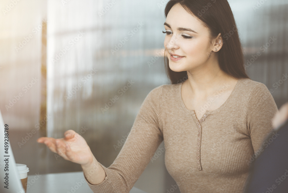 Young business people are talking to each other, while sitting at the desk in sunny office. Businesswoman is explaining something to her colleague