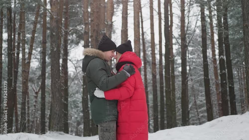 Portrait of lovely man and woman hugging in winter forest. Happy young couple dating outdoors. Man embracing woman in red coat. Relationship concept. 4K, UHD Portrait of lovely man and woman hugging in winter forest. Happy young couple dating outdoors. Man embracing woman in red coat. Relationship concept. 4K, UHD