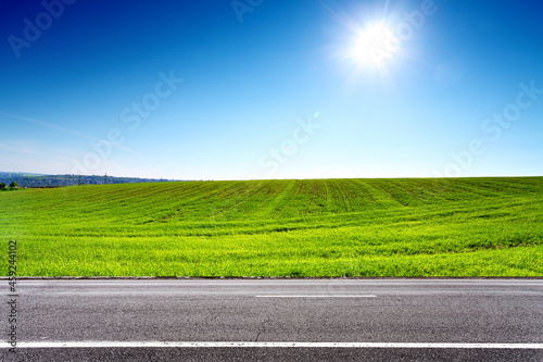 Road and green field with sun on blue sky