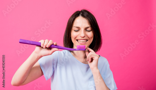 Beautiful happy young woman with big toothbrush on blank pink background