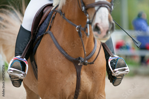 Croup of a red horse with a saddle and a rider’s foot in a boot with a spur inserted in a stirrup.