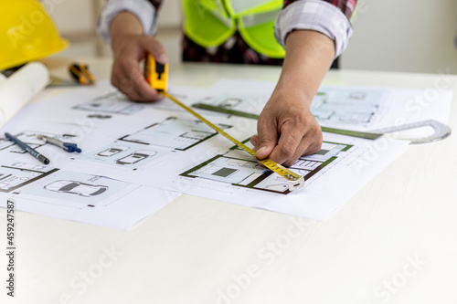 The male architect uses a tape measure to measure the house designs, he is checking the house plans that he has designed before sending it to the customers, he designs the house and the interior.