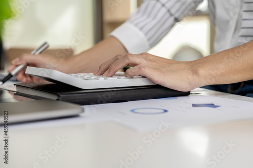 financial business woman pressing a white calculator, she uses a calculator to calculate the numbers in the company's financial documents that employees in the department create as meeting documents. © kamiphotos