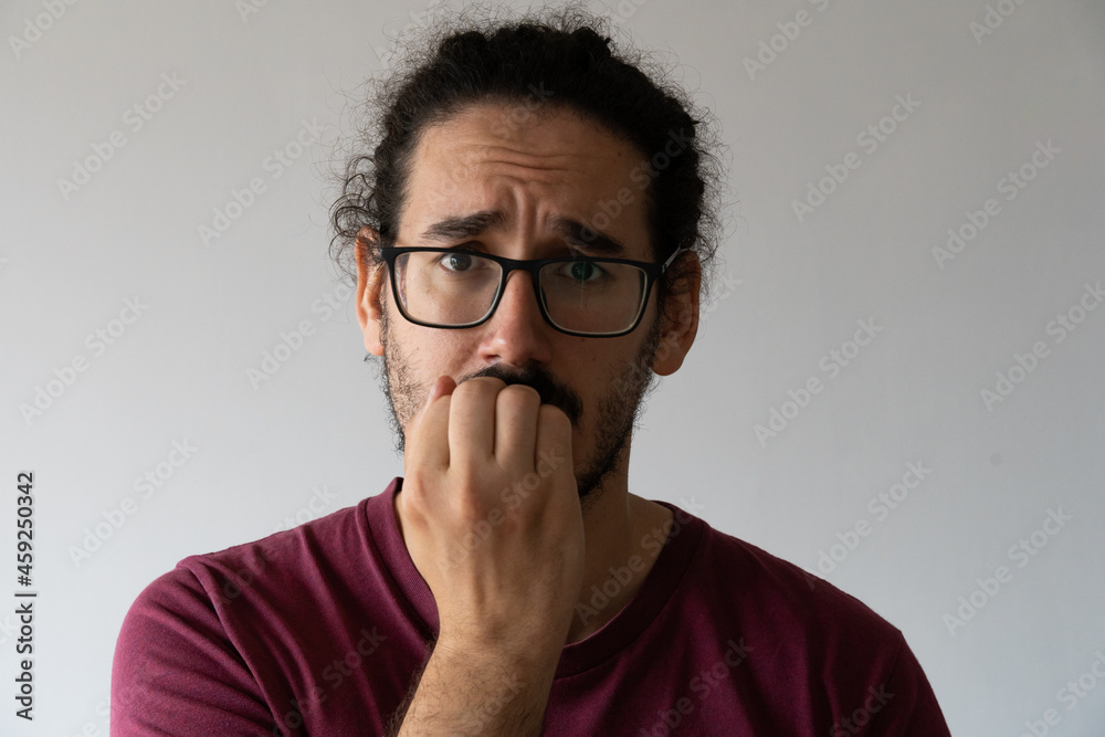 Close up of anxious young man biting his nails and looking at the camera