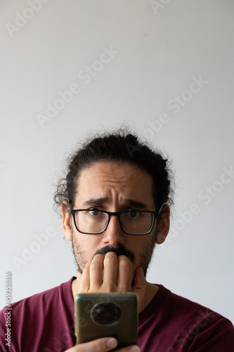 Vertical close up of anxious man with smartphone biting his nails and looking at camera