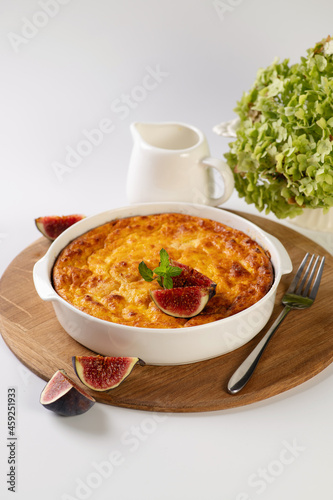 curd casserole with pumpkin in a round white shape on a wooden board to serve on a white table, vertical format photo