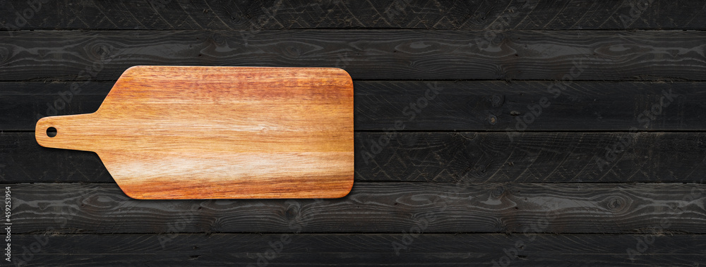 Wooden cutting board isolated on black wood background. Horizontal banner