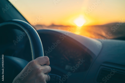 Fototapeta Naklejka Na Ścianę i Meble -  Female hands of car driver on steering wheel, road trip at sunset