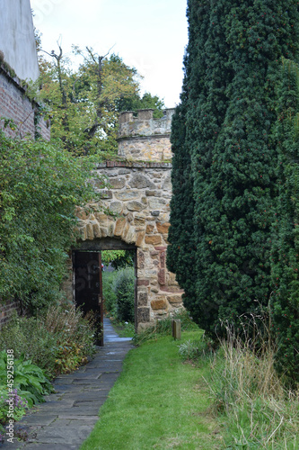 Fototapeta Naklejka Na Ścianę i Meble -  Narrow Path & Garden with Open Doorway in Old Stone Wall 