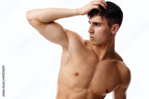 confident man athlete with a pumped-up torso touches his head with his hand on a light background