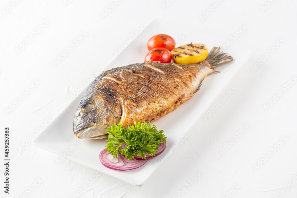 Fried dorado fish with lemon, grilled tomatoes, herbs and red onion rings on a white plate Fried dorado fish with lemon, grilled tomatoes, herbs and red onion rings on a white plate