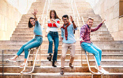 Multiethnic friends walking down stairs with stupid funny moves - Happy guys and girls having fun at urban city center on party mood - College students in travel holidays  - Bright warm filter photo