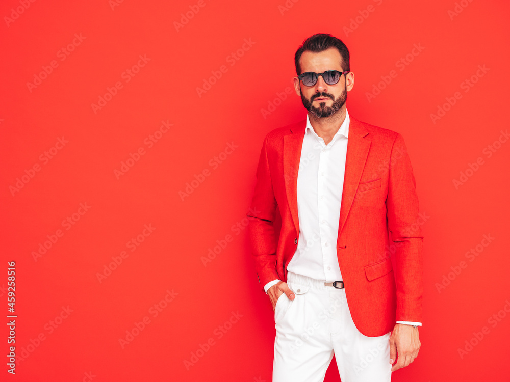 Portrait of handsome confident stylish hipster lambersexual model. Sexy modern man dressed in elegant suit. Fashion male posing in studio near red wall in sunglasses Portrait of handsome confident stylish hipster lambersexual model. Sexy modern man dressed in elegant suit. Fashion male posing in studio near red wall in sunglasses