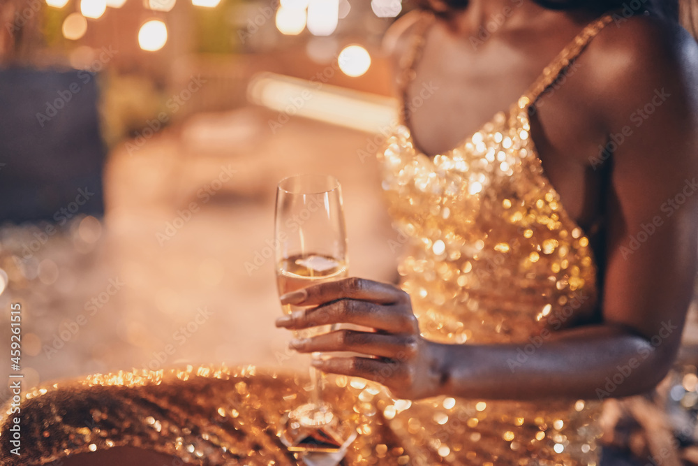 Close-up of beautiful young African woman in evening gown holding flute with champagne - obrazy, fototapety, plakaty 