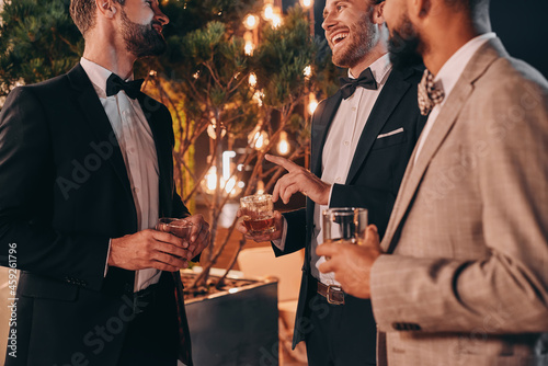 Close-up of three well-dressed men drinking whiskey and communicating while spending time on party photo