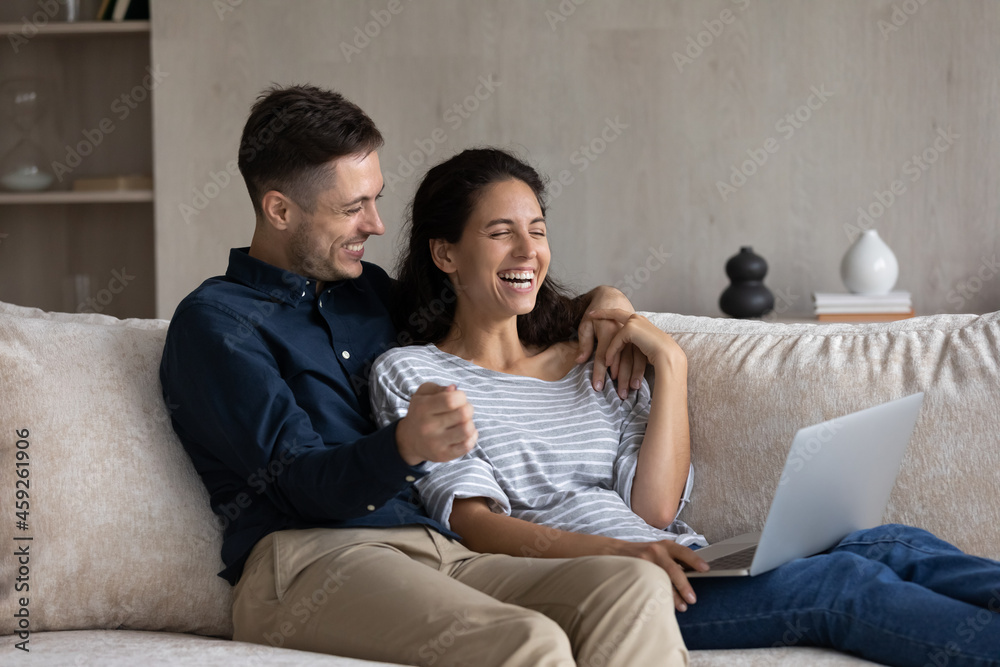 Happy affectionate laughing young family couple using computer, watching  funny comedian movie or online video content in social network, buying  goods on services, playing games, relaxing at home. Stock Photo | Adobe