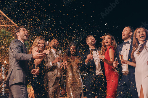 Canvas Print Group of happy people in formalwear having fun together with confetti flying all
