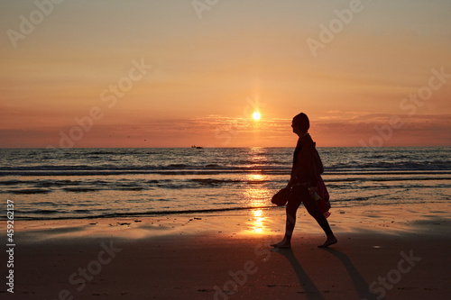A silhouette of a person walking on a sea shore at sunset