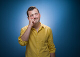 Strict young man thinks. Portrait of doubtful guy with confusion face expression over blue background, dresses in yellow shirt. Careful man, copy space for text