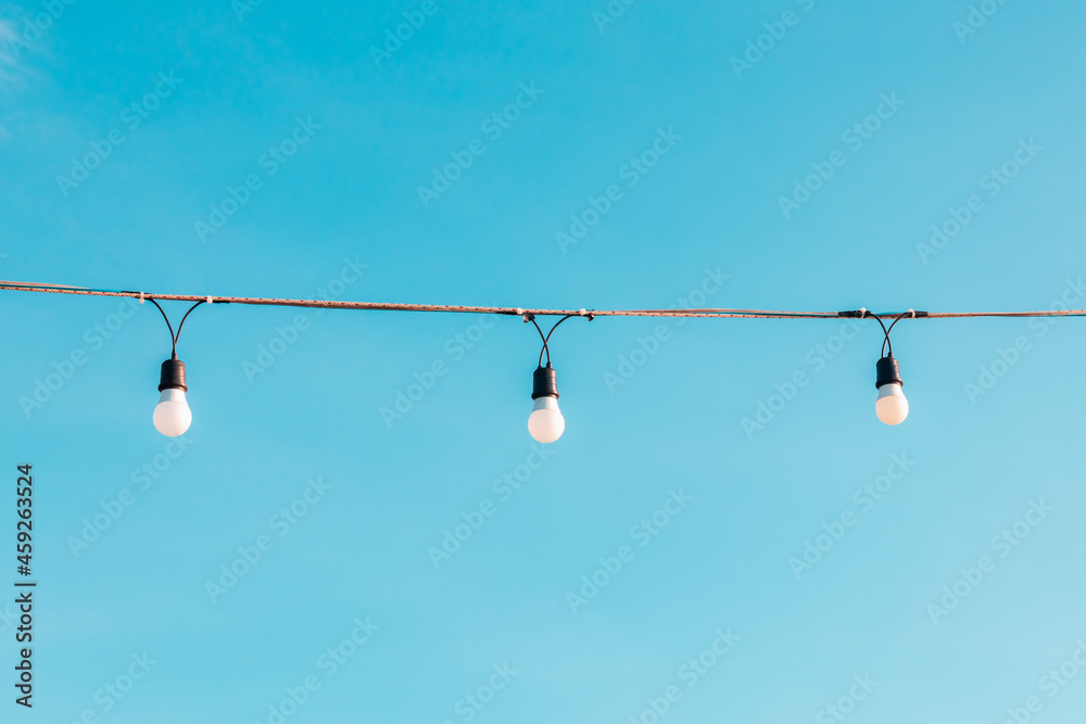 Three light bulbs are hung on a string at the festival with a bright pastel blue sky that looks creative, giving a feeling of freedom on fine weather days. Three light bulbs are hung on a string at the festival with a bright pastel blue sky that looks creative, giving a feeling of freedom on fine weather days.