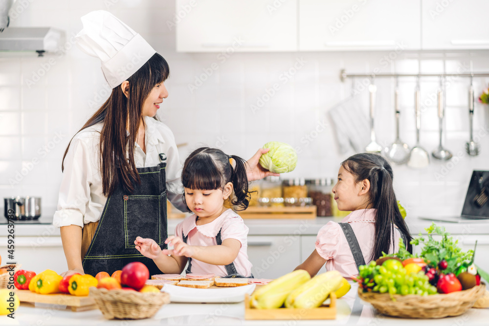 Portrait of enjoy happy love asian family mother and little asian girl daughter child having fun cooking together with fresh vegetable salad and sandwich ingredients on table in kitchen Portrait of enjoy happy love asian family mother and little asian girl daughter child having fun cooking together with fresh vegetable salad and sandwich ingredients on table in kitchen
