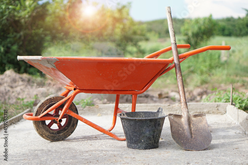 Orange wheel barrow cart trolley , bucket and shovel  that use for construction to carry cement mixture at worksite. Concept : Construction worker's  tool.          photo