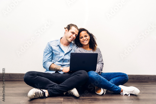 Romantic young happy love couple caucasian man and african american woman smile and have fun relax use technology together of laptop computer work and checking social apps on wall background