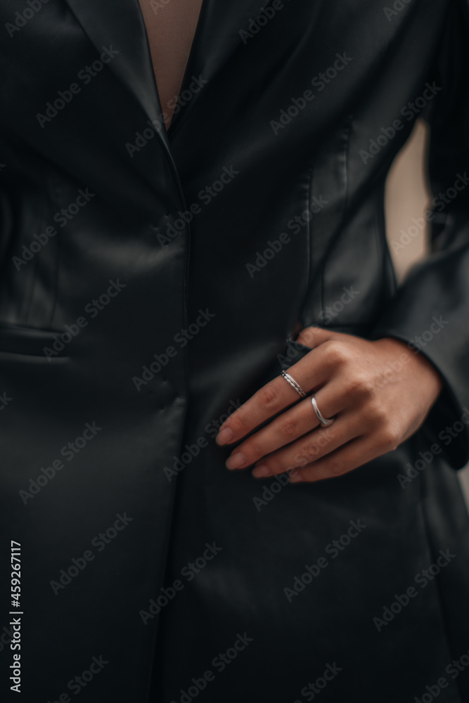 Female hands with silver rings in the pockets of a black long leather jacket. Style, design of women's clothing. Vertical