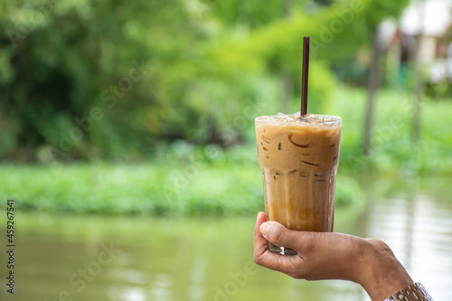 Glass of cold espresso coffee in hand Background blurry views tree and water