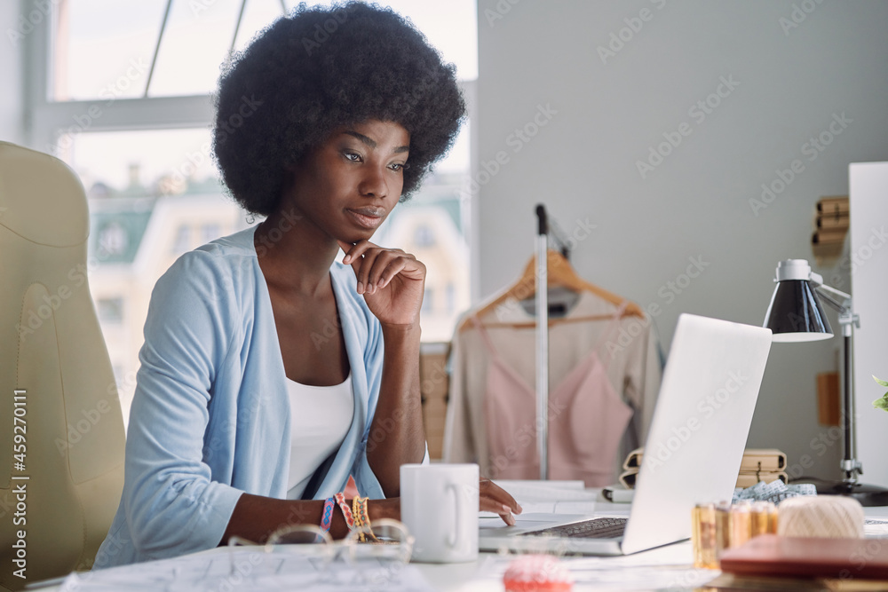 Beautiful young African woman using laptop while working in design studio Beautiful young African woman using laptop while working in design studio