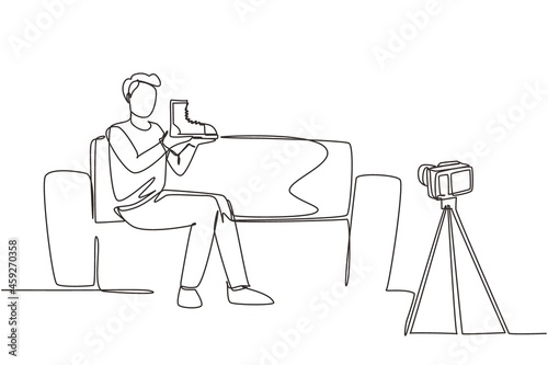 Single one line drawing social media influencer reviewing boots. Smiling young man vlogging about men's sports shoe and filming himself at home on a video camera. Continuous line draw design vector