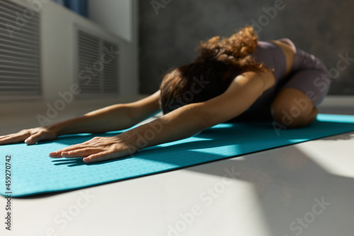Horizontal crop shot of woman lying in Adho Mukha Virasanna position for spine lengthening, shoulders opening, lower back releasing, opening shoulders, mental and physical relaxation