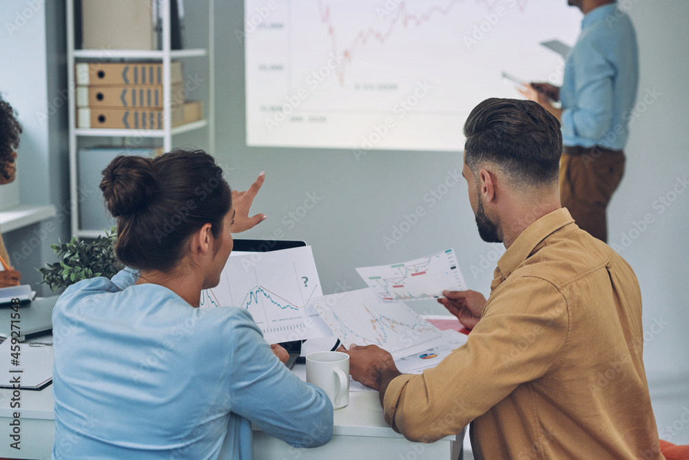 Obraz premium Group of young modern people in smart casual wear analyzing data on projection screen in the office