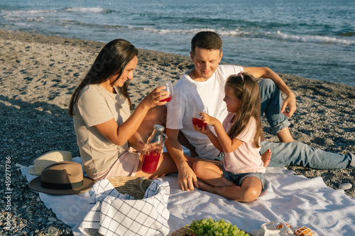 Family spending time together outdoor. Summer leisure picnic lunch with fruits by the seaside. Happy people eating healthy food and sitting on blanket on the beach.