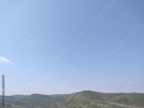 Small green hill under light blue cloudless sky in ravine