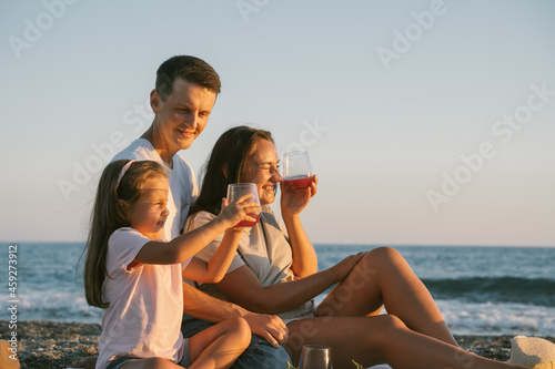 Family spending time together outdoor. Summer leisure picnic lunch with fruits by the seaside. Happy people eating healthy food and sitting on blanket on the beach side view banner. © valeriyakozoriz