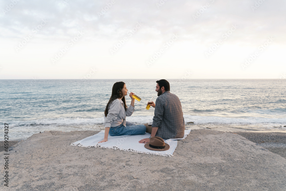 Couple enjoying seaside view, drinking beer alone. Portrait of happy people spending time picnic leisure together on the sunset.
