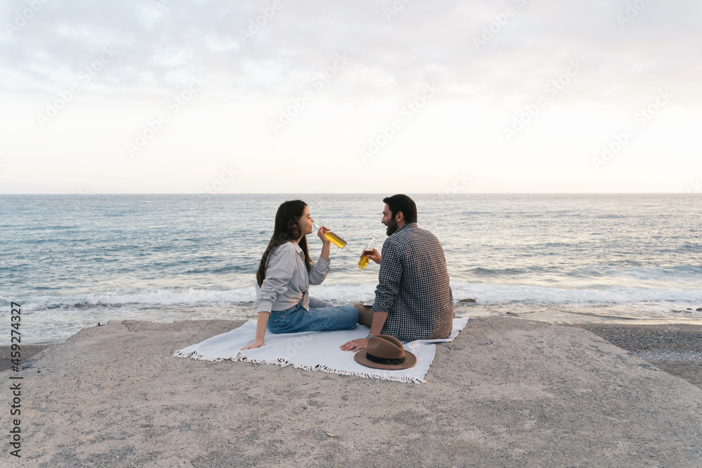 Couple enjoying seaside view, drinking beer alone. Portrait of happy people spending time picnic leisure together on the sunset. Couple enjoying seaside view, drinking beer alone. Portrait of happy people spending time picnic leisure together on the sunset.