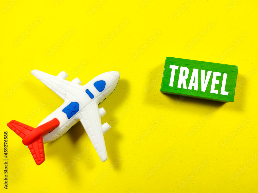 A airplane toy written with text TRAVEL on colored wooden cube on a yellow background. Holiday and travel concept.