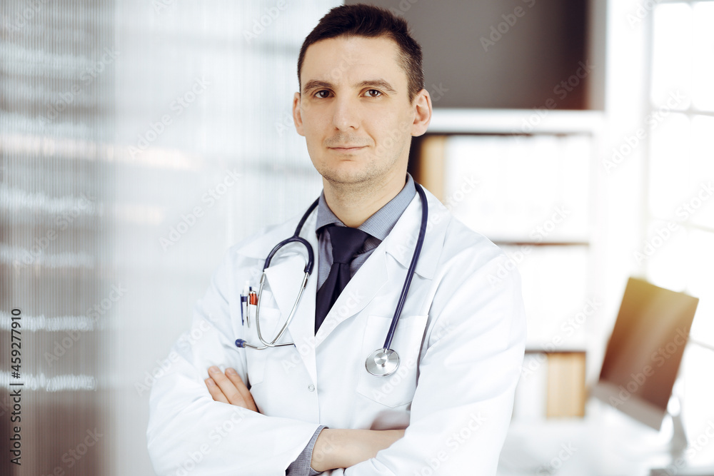 Male doctor standing straight in sunny clinic. Perfect medical service in hospital Male doctor standing straight in sunny clinic. Perfect medical service in hospital