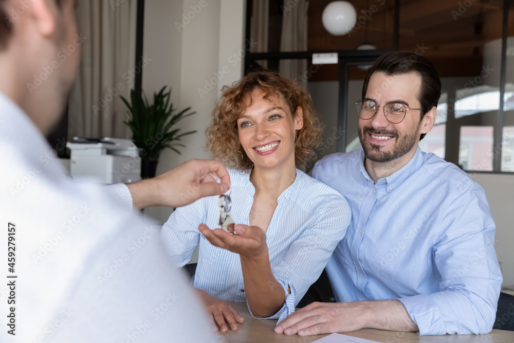 Real estate agent giving key from new house to happy family couple of customers, rented apartment. Clients and realtor, property seller meeting in office for property rent or buying deal