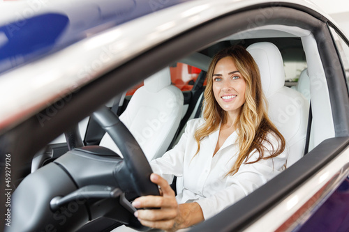 Happy driver woman 20s customer buyer client in shirt hold put hand on steering wheel choose auto want buy new automobile in car showroom vehicle salon dealership store motor show indoor Sale concept