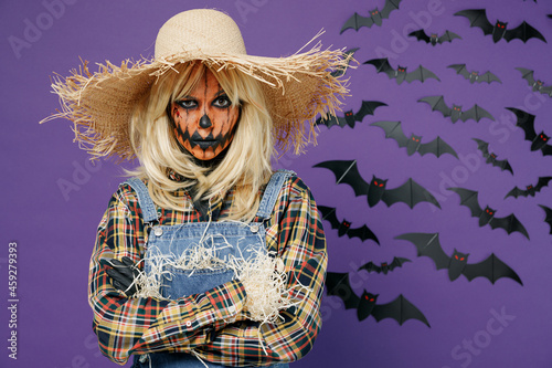 Young woman 20s with Halloween makeup mask in straw hat denim scarecrow costume look camera hold hands crossed folded isolated on plain dark purple background studio Celebration holiday party concept. photo