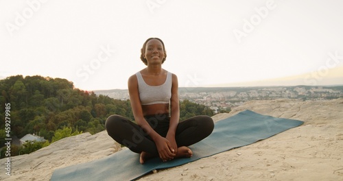 Young multiracial woman sitting in yoga posture and meditating at the mountains. Girl performing aerobics exercise and morning meditation at the nature. Physical and spiritual practice concept