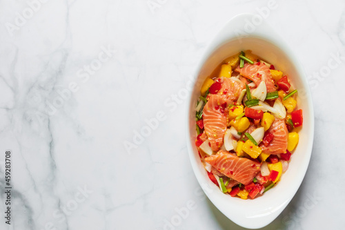 Spicy salmon mango salad in white oval bowl. Top view on white table with copy space.
